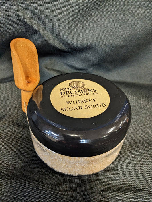 A black jar with a wooden lid labeled 'Pour Decisions Distillery Sugar Scrub'.